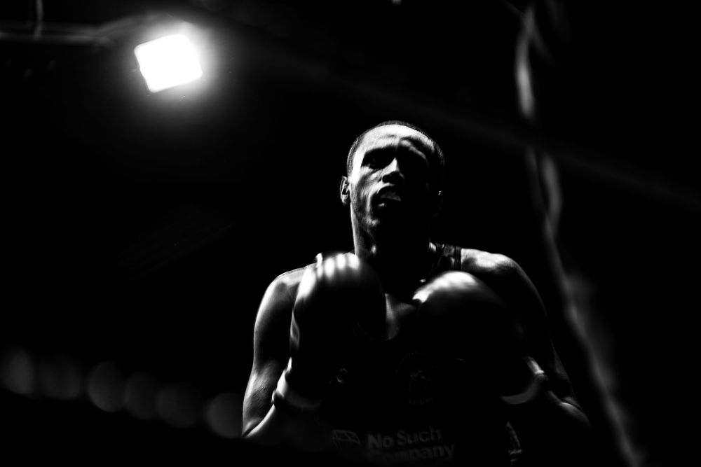 A boxer shouts intensely under dramatic spotlight in a black and white boxing match photo.