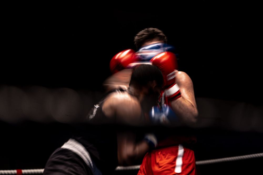 Two boxers sparring in a boxing ring, wearing red and blue gloves under dramatic dark lighting.