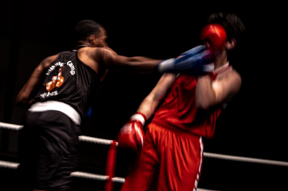 Two boxers exchange punches in a boxing ring, captured with motion blur during an intense match.