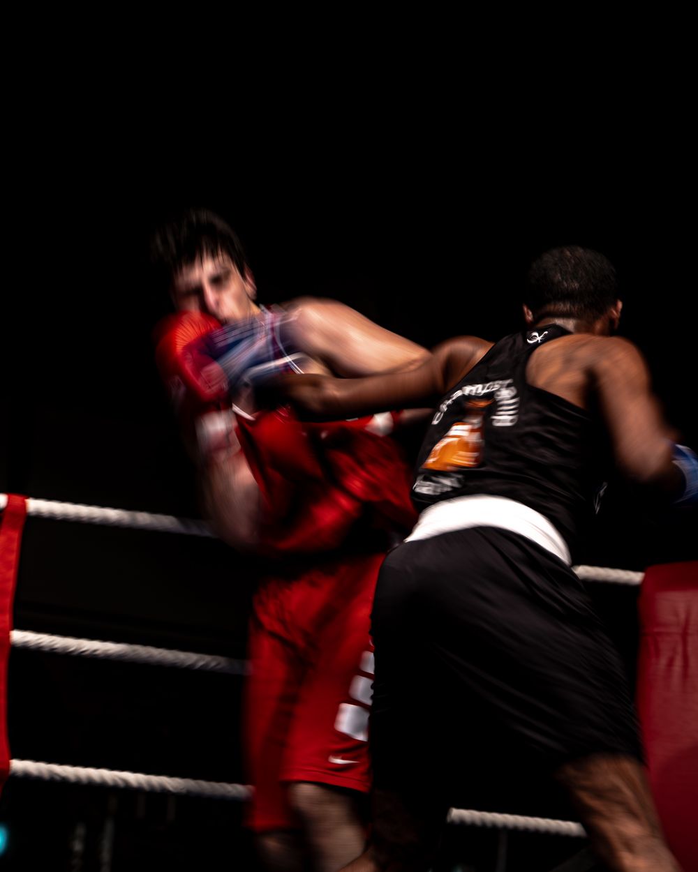 Two boxers exchange punches in a boxing ring, captured with motion blur highlighting the intensity of the fight.