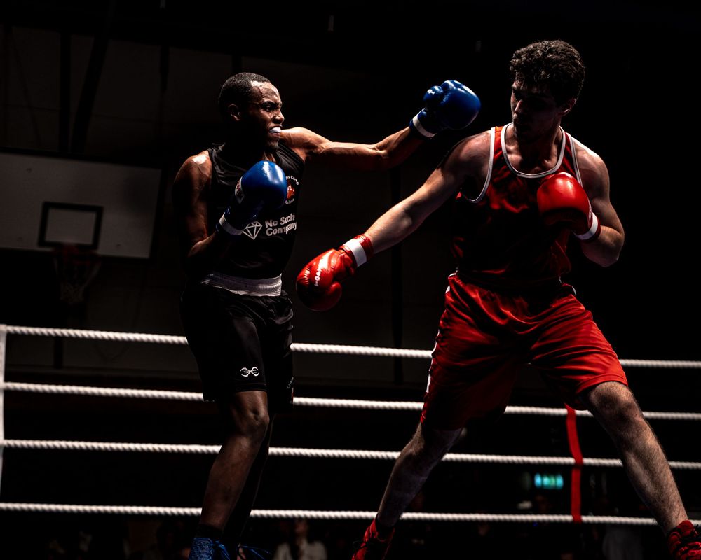 Two boxers sparring in a ring, one in blue gloves and one in red gloves, mid-punch during an intense match.