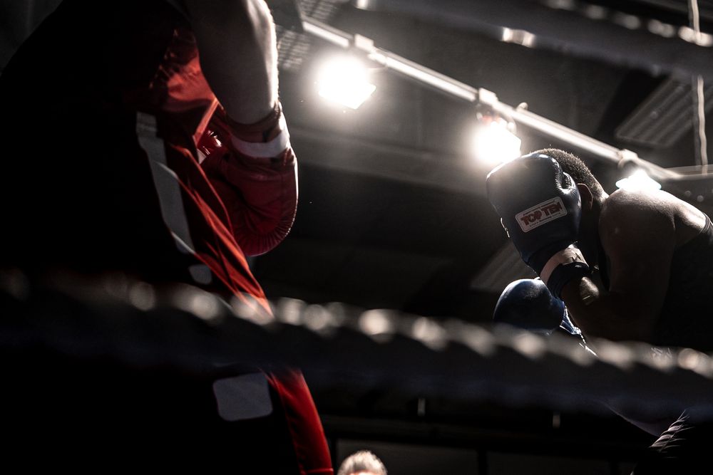 Two boxers exchange punches under bright ring lights during an intense boxing match.