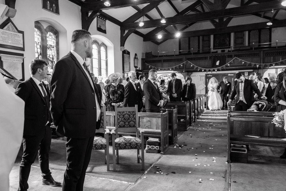 Black and white wedding ceremony photo inside a church with guests seated in pews and the couple at the altar.