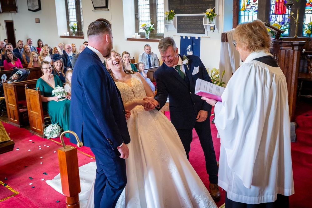 Father of the bride gives away his daughter during a traditional church wedding ceremony with guests watching.