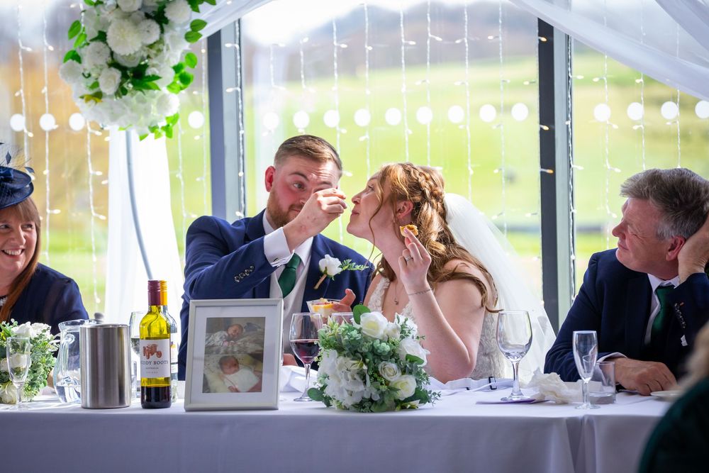 Bride and groom share a tender moment at wedding reception table with white floral decorations.
