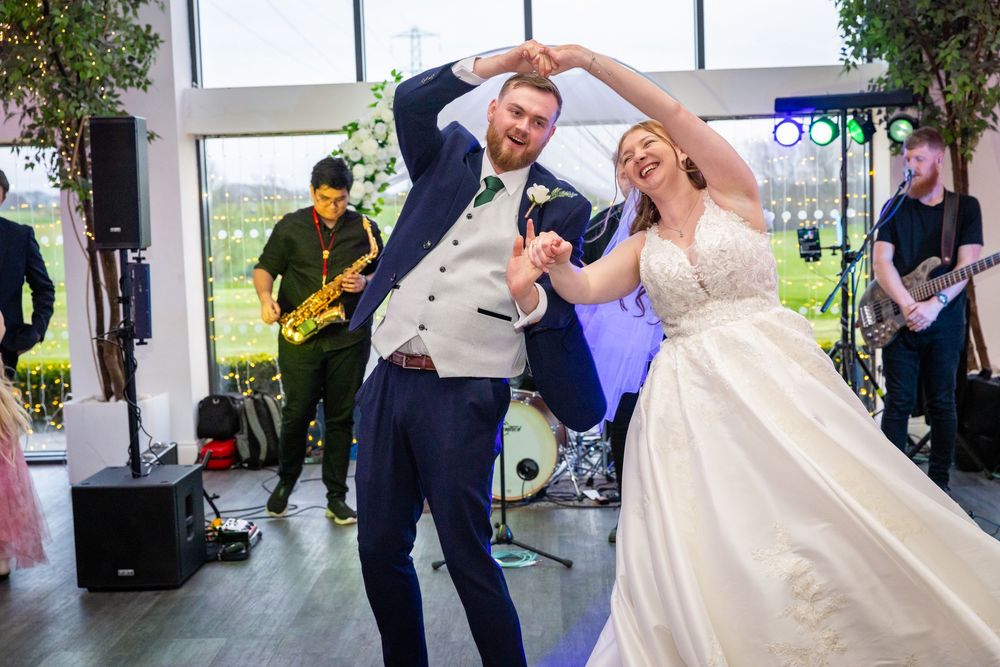 Bride and groom share first dance at wedding reception with live band performing in background.