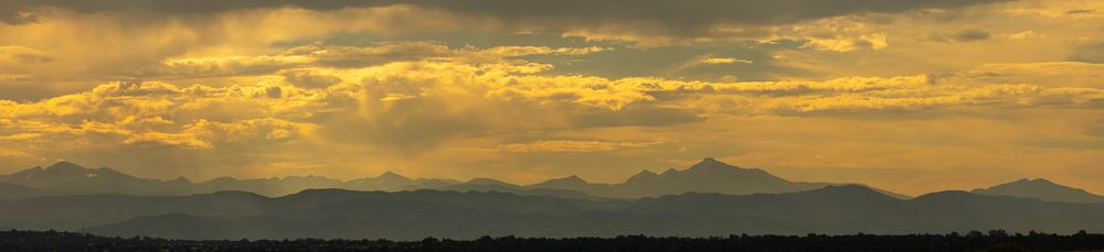 Wide panoramic view of mountain range silhouettes beneath a dramatic golden sunset sky.