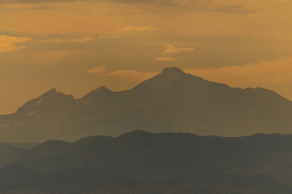 Layered mountain peaks bathed in warm golden orange hues during a stunning sunset.