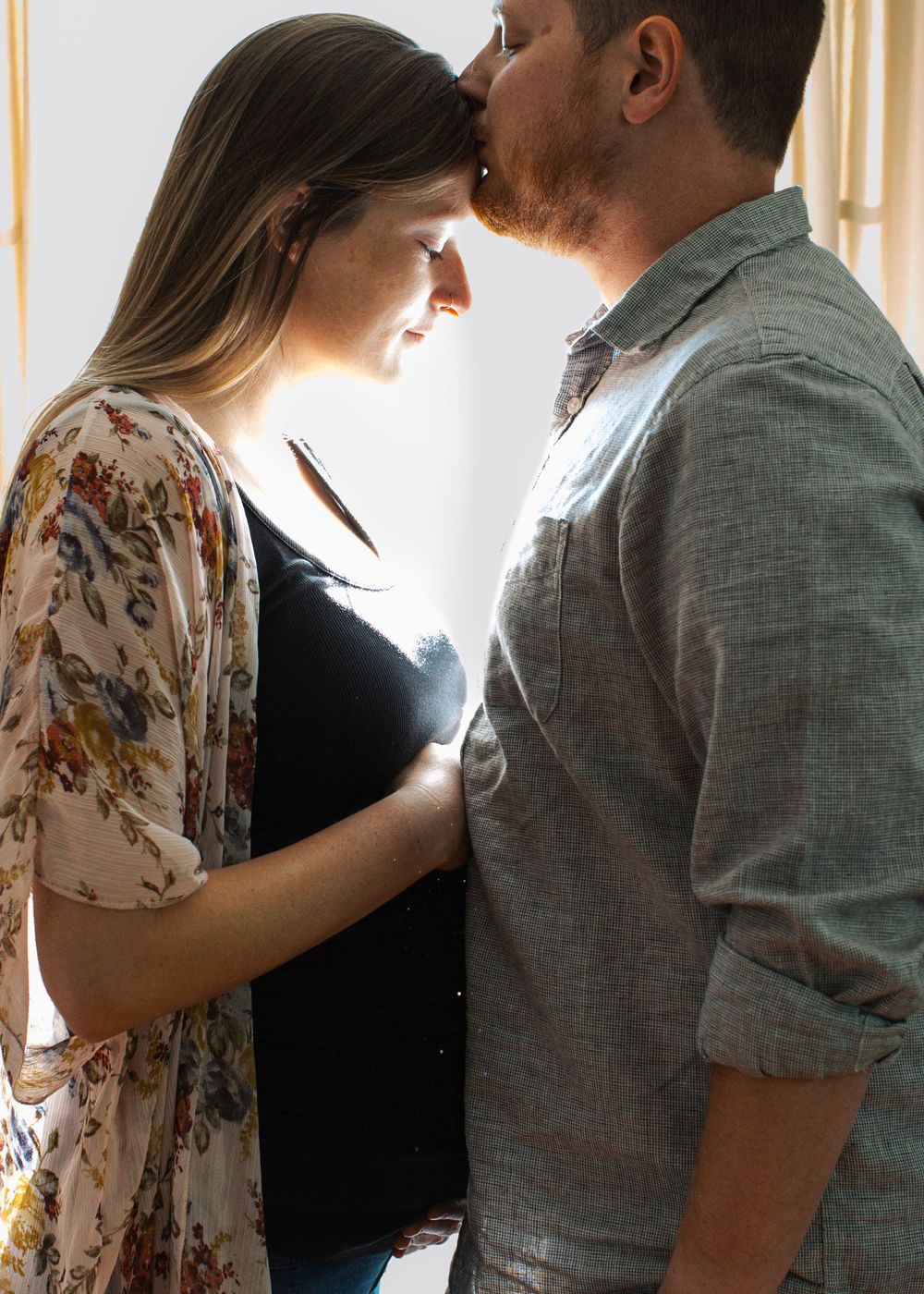 Couple embracing with beautiful surrounding light during their in-home maternity session in Flint, Michigan