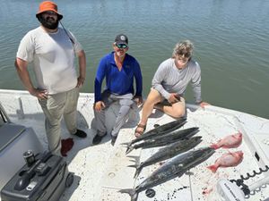 Three anglers pose on a boat with their fresh catch of kingfish and red snapper after a successful offshore fishing trip.