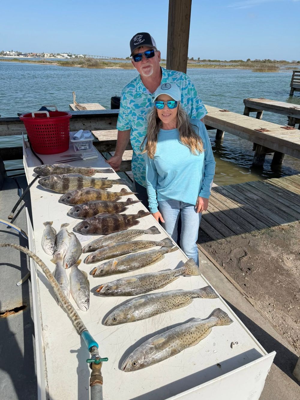 Couple poses with a impressive catch of speckled trout and flounder on a Texas fishing dock.
