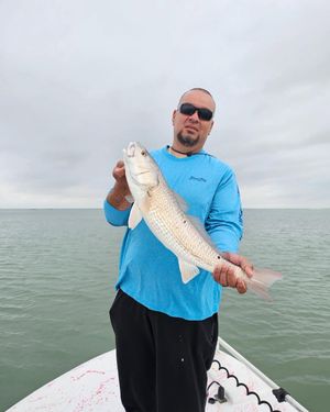 Angler in blue shirt holds a redfish caught on a Texas bay fishing charter on cloudy day.