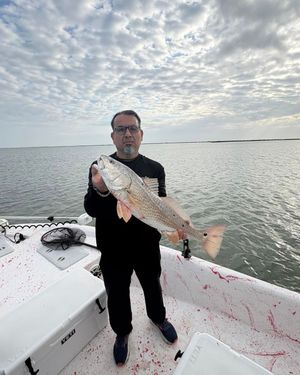 Fisherman displays a large redfish on a boat deck under dramatic cloudy skies on Texas bay.