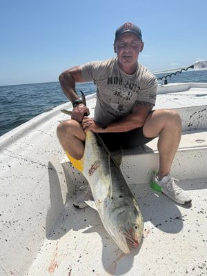 Angler sits on boat deck holding a large yellowfin tuna with yellow fins visible offshore.