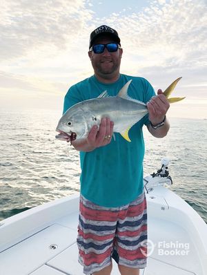 Smiling angler holds a jack crevalle fish on a white center console boat at sunset.