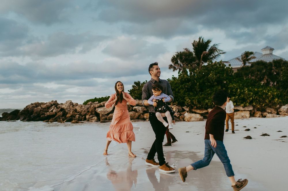 Happy family walks along a tropical beach at sunset with palm trees in background.