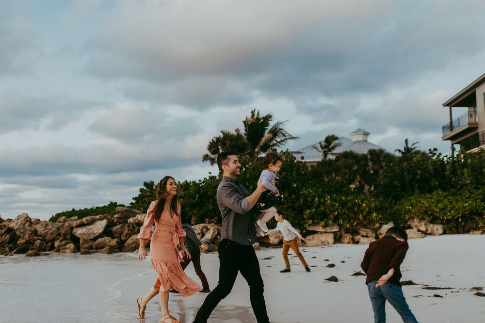Family walking on a tropical beach at sunset, with palm trees and rocky shoreline in the background.