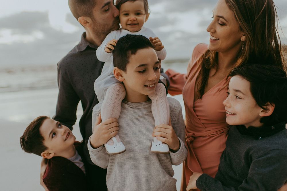 Happy family of six smiling together on a beach, with children and parents enjoying time outdoors.