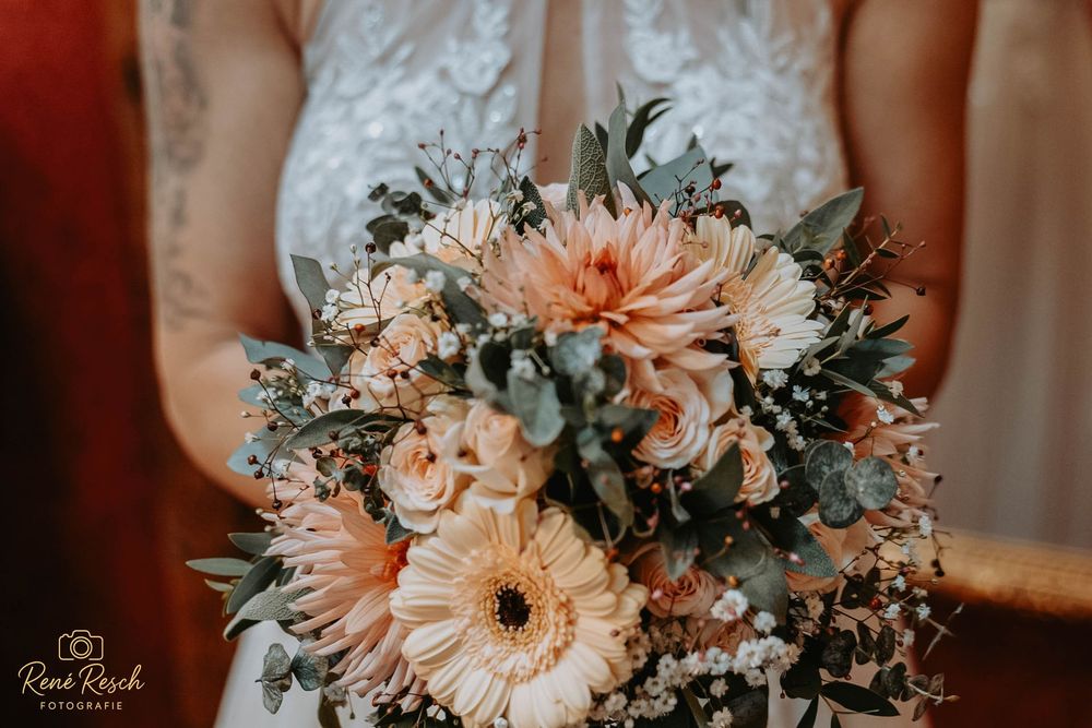 Bride holding a romantic bridal bouquet with peach dahlias, gerberas, roses, and eucalyptus greenery.
