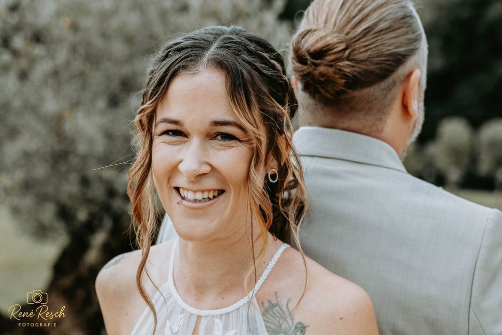 Smiling bride with braided updo and tattoo at outdoor wedding ceremony, photographed by Rene Rasch.