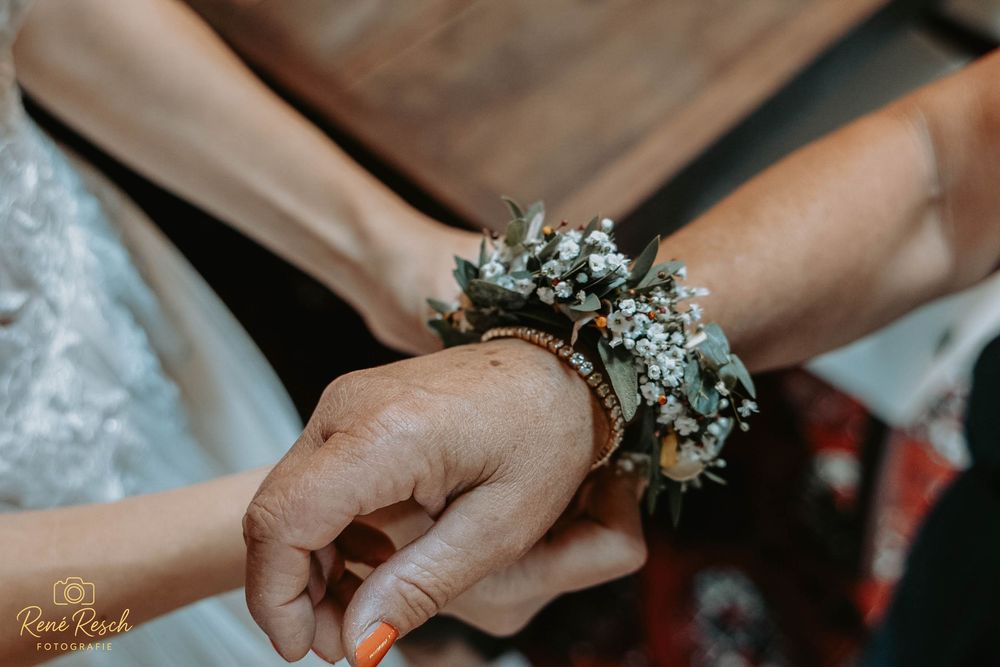 Close-up of a bride placing a floral wrist corsage on an older woman's hand at a wedding ceremony.
