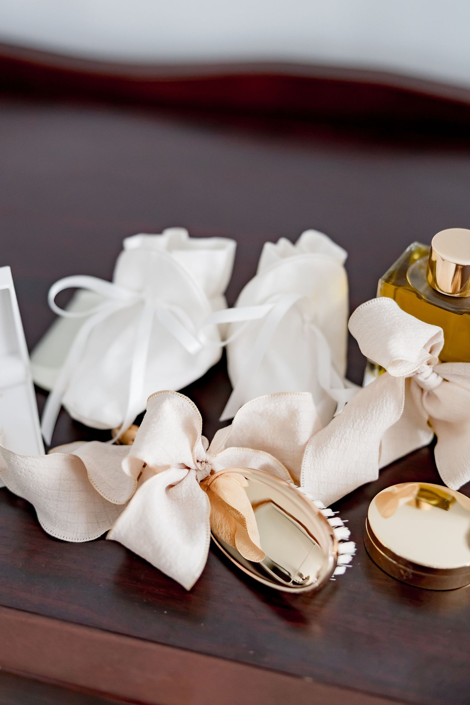 White ribbon wedding favors and gold perfume bottle arranged on dark wooden surface for bridal preparation.
