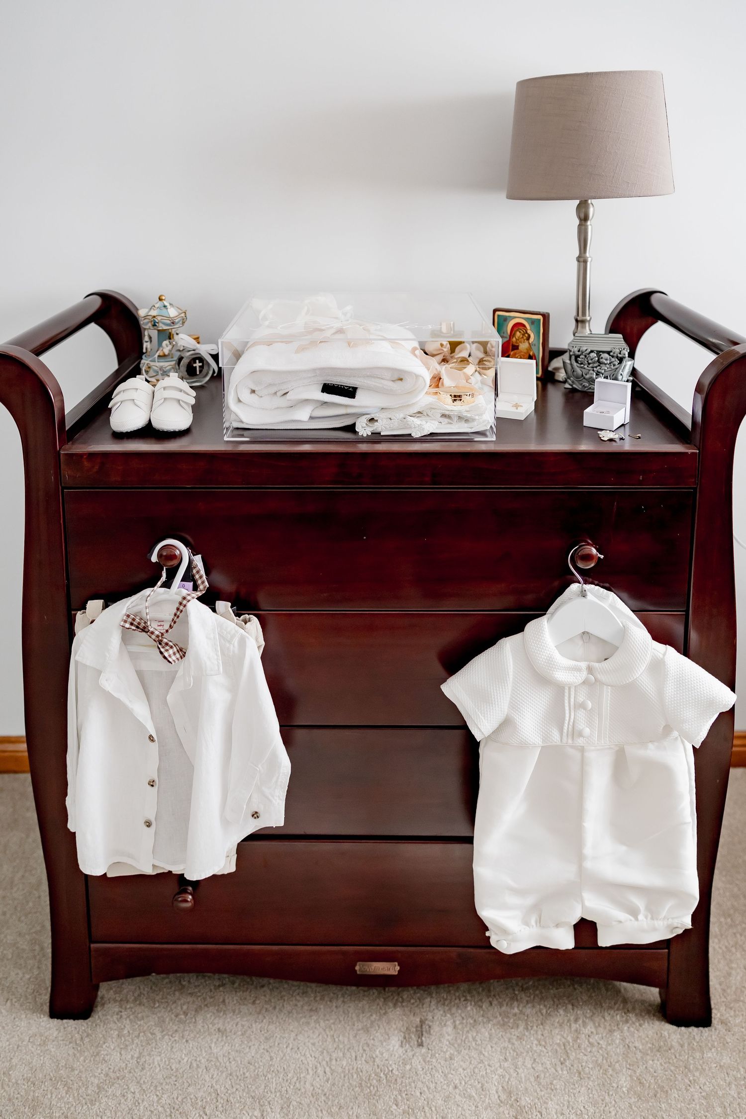 Dark wood dresser with white baby christening outfits hanging on hangers.