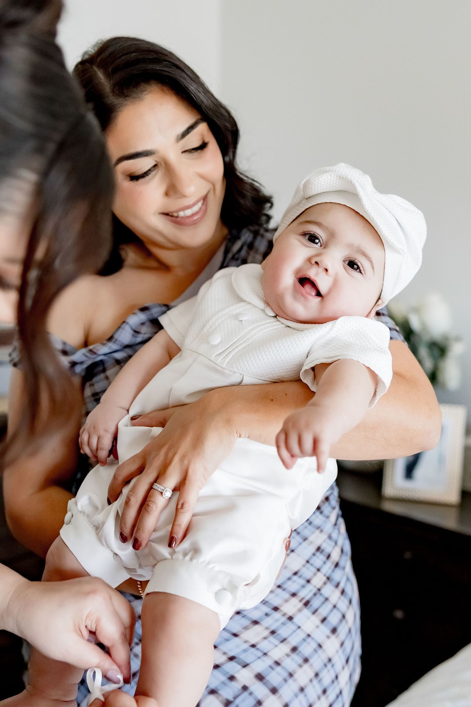 Smiling mother holding her happy baby dressed in a white christening outfit and cap.