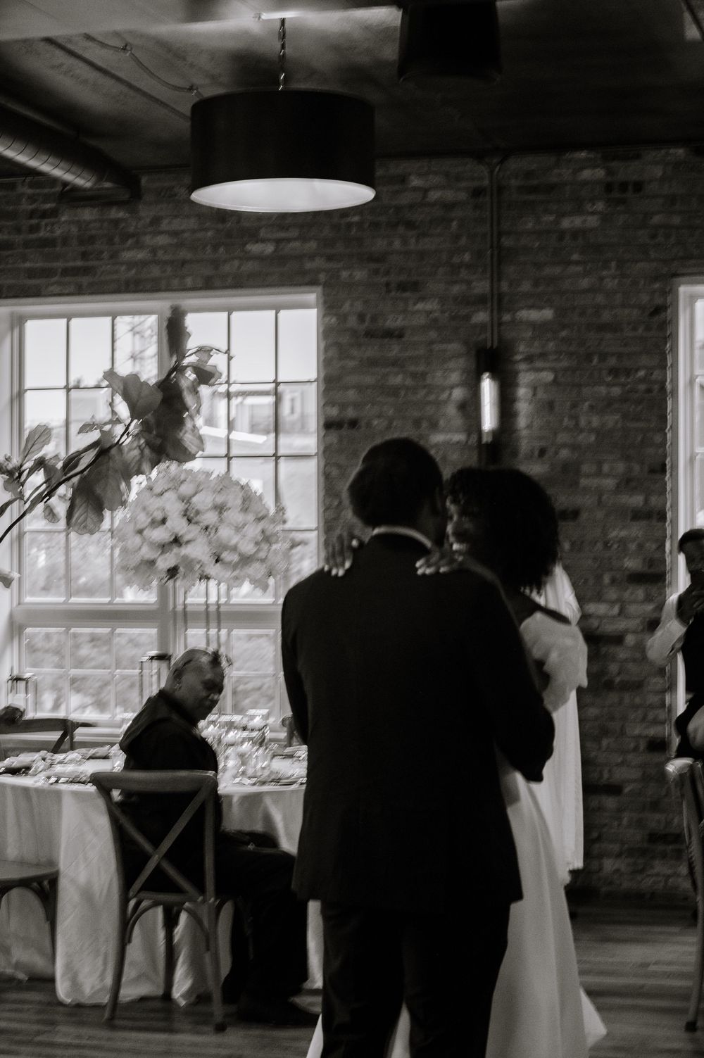 Black and white photo of bride and groom sharing a moment at their wedding reception in a brick venue.