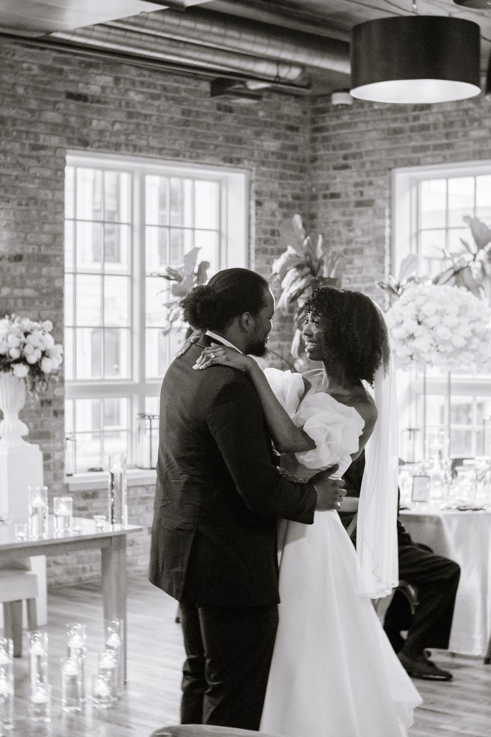 Black and white photo of a bride and groom sharing their first dance at an elegant wedding reception with brick walls.