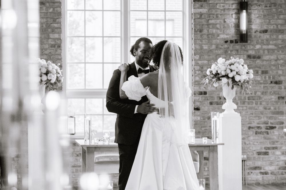 Black and white photo of a couple sharing a tender moment at a wedding ceremony in a brick chapel.