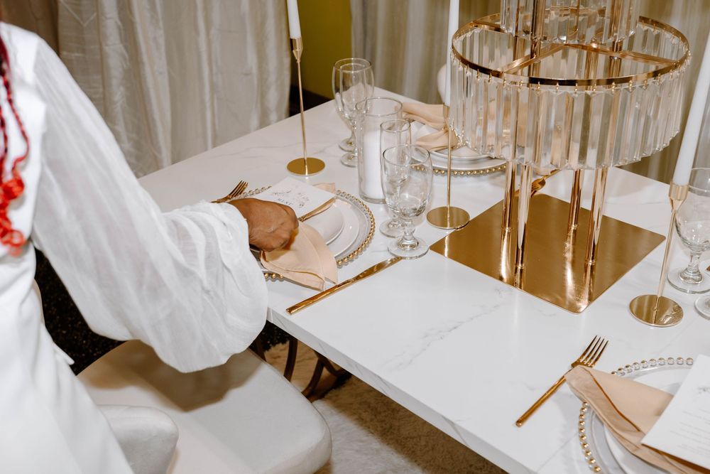 Person setting a white marble table with gold cutlery and crystal glassware for an elegant event.