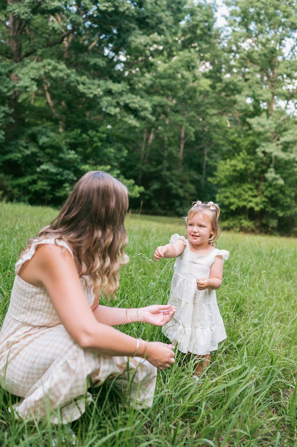 Mother crouching in tall grass playing with her smiling toddler daughter outdoors Greensboro NC