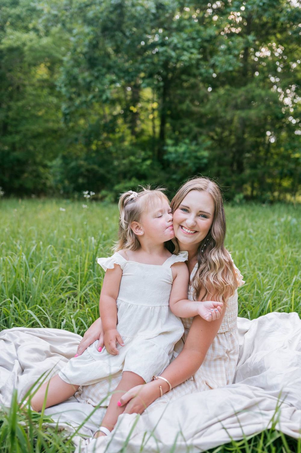 Toddler girl kissing her mother on the cheek while sitting together on a blanket in a green field Lexington NC