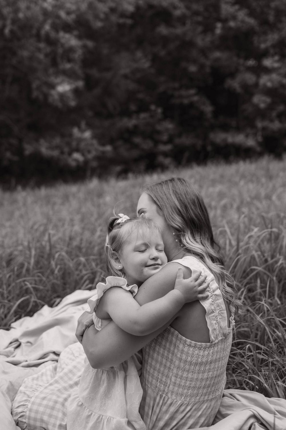 Black and white photo of a mother and toddler daughter sharing a warm embrace in a grassy field in North Carolina