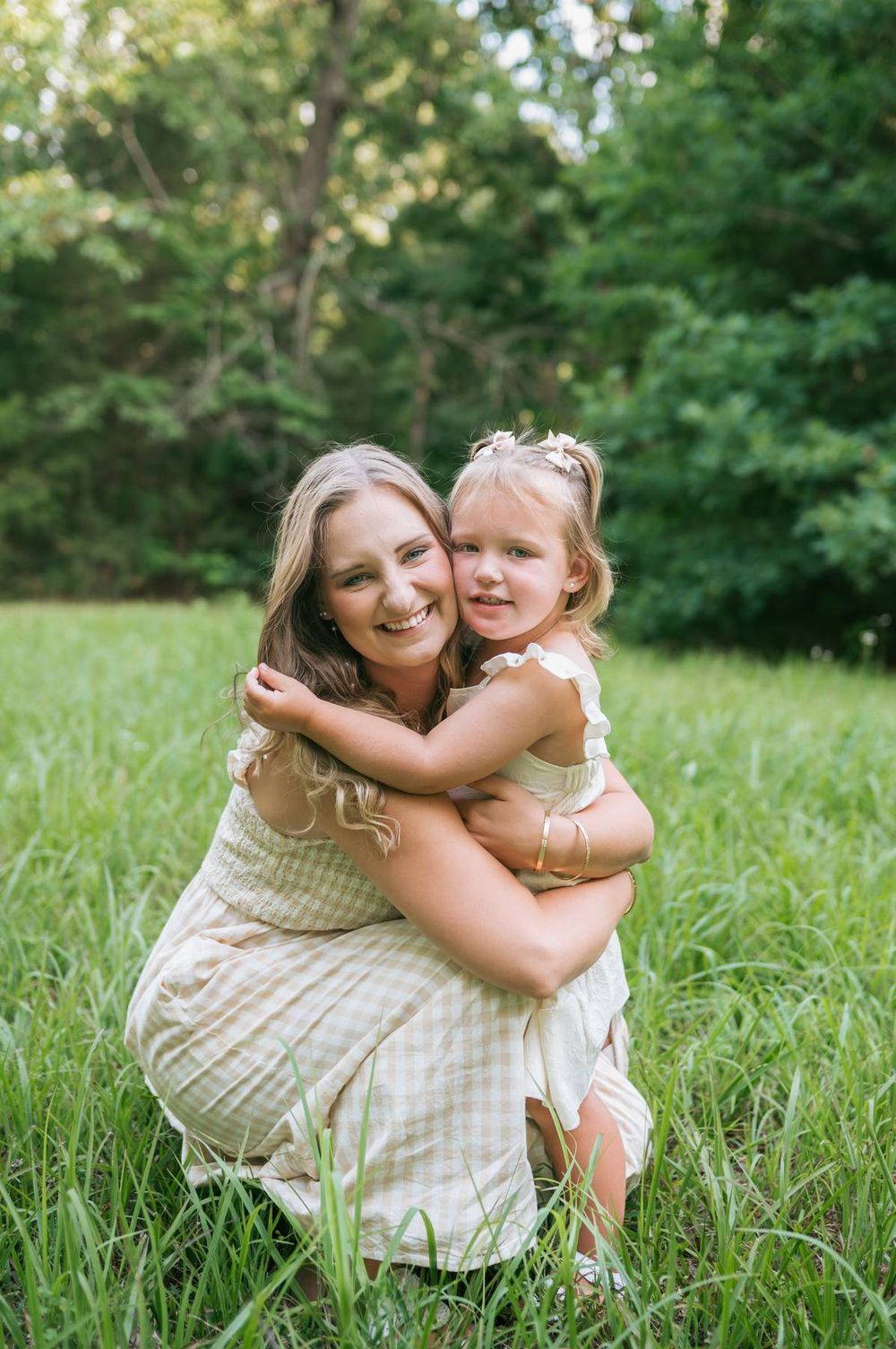 Mother hugging her toddler daughter while kneeling in a green grassy field outdoors Lexington NC