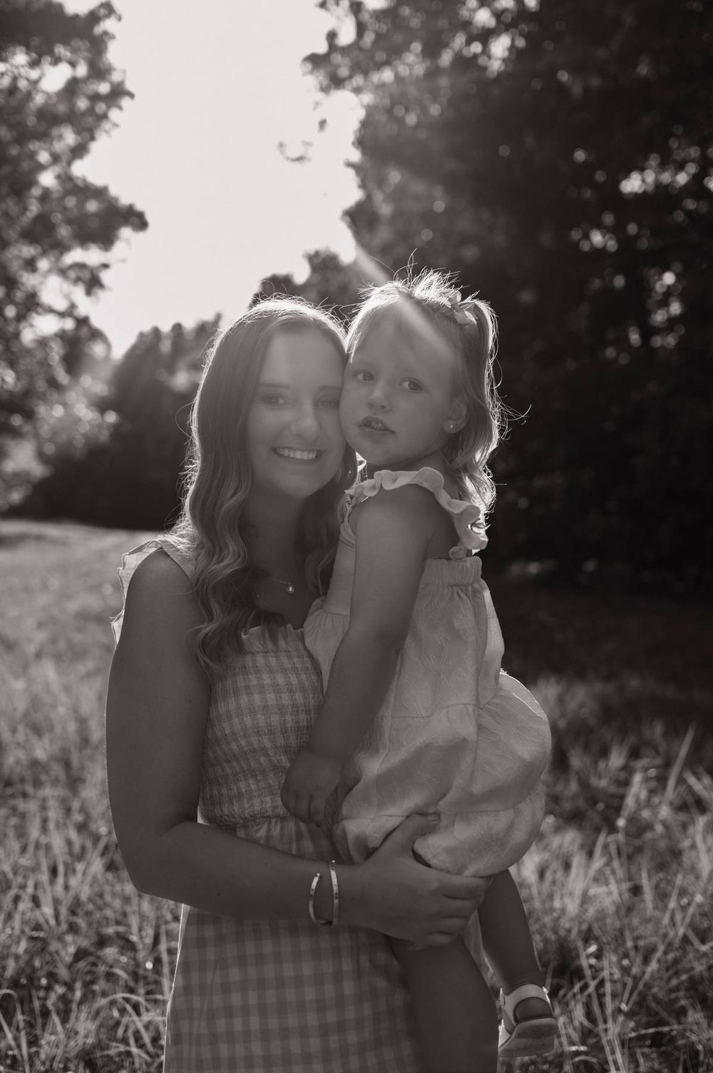 Black and white portrait of a mother holding her toddler daughter in a sunlit outdoor setting Greensboro NC