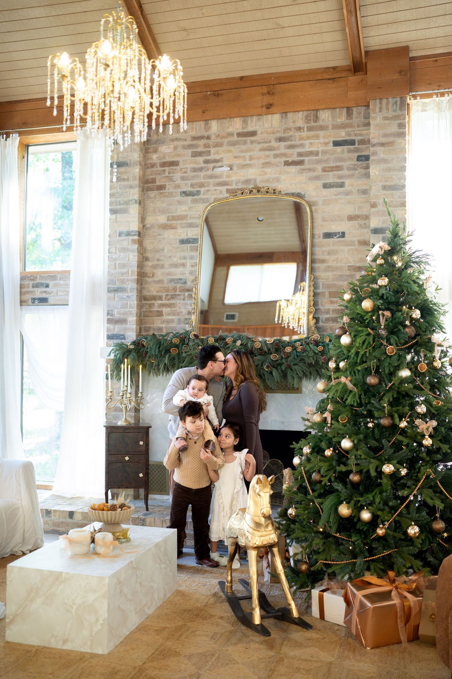Family celebrating Christmas near decorated tree with gifts, rocking horse, and fireplace in elegant living room.