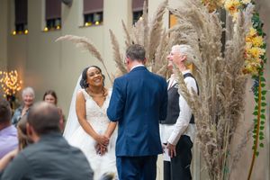Bride smiling joyfully at groom during wedding ceremony with pampas grass floral arch decor.  Quad Cities Wedding Photographer