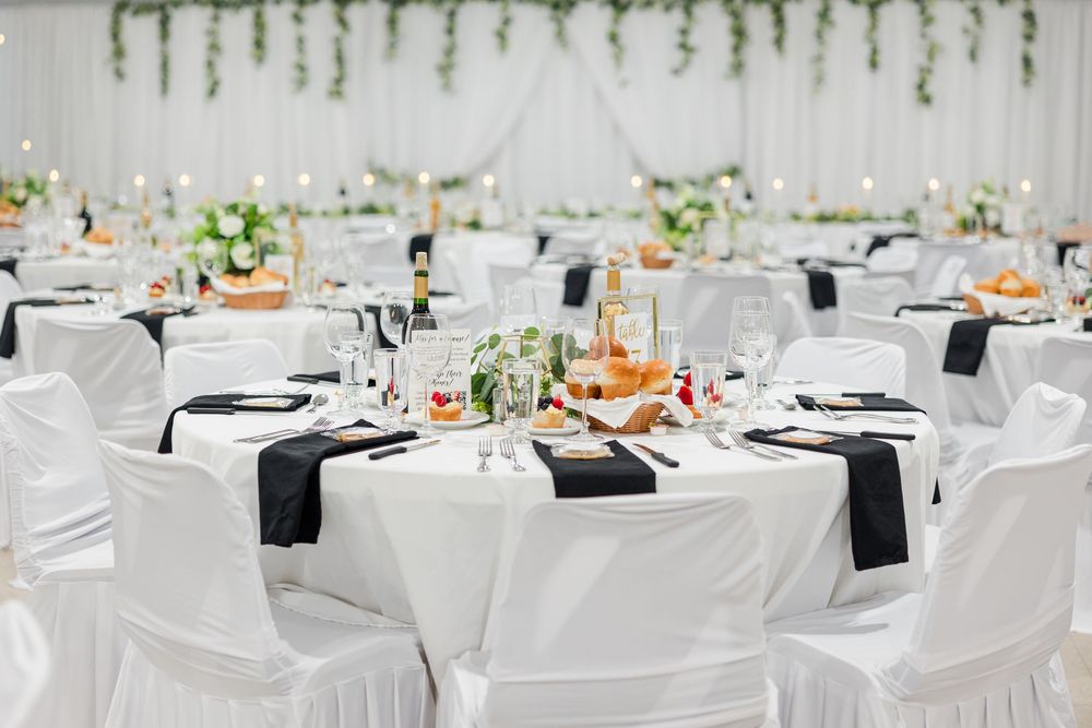 Elegant wedding reception hall with white chair covers, black satin sashes, and floral centerpieces on round tables.