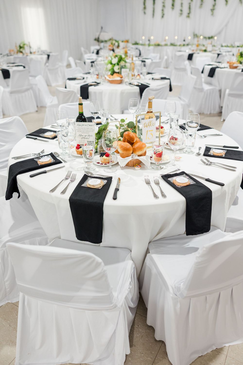Elegant wedding reception hall with round tables draped in white linens and black runners, set with glassware and floral centerpieces.