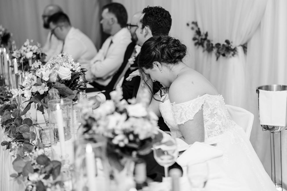 Bride reads notes at wedding reception head table in elegant black and white photo.