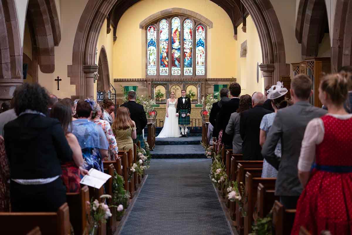 A wedding ceremony in a traditional church with guests seated in wooden pews as the couple stands at the altar.