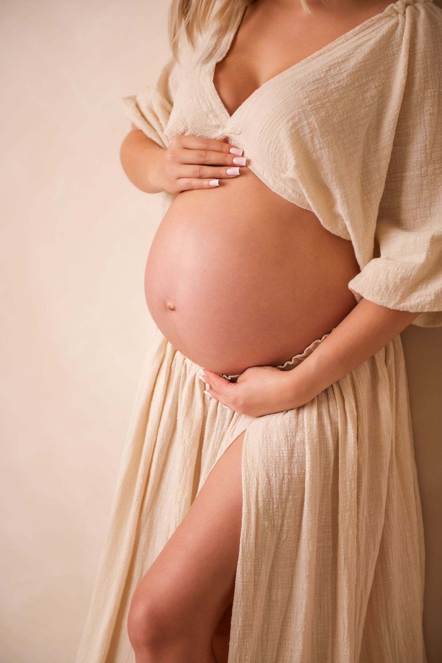 A sleeping baby wrapped in soft beige fabric lies peacefully against a neutral backdrop in a professional portrait setting.