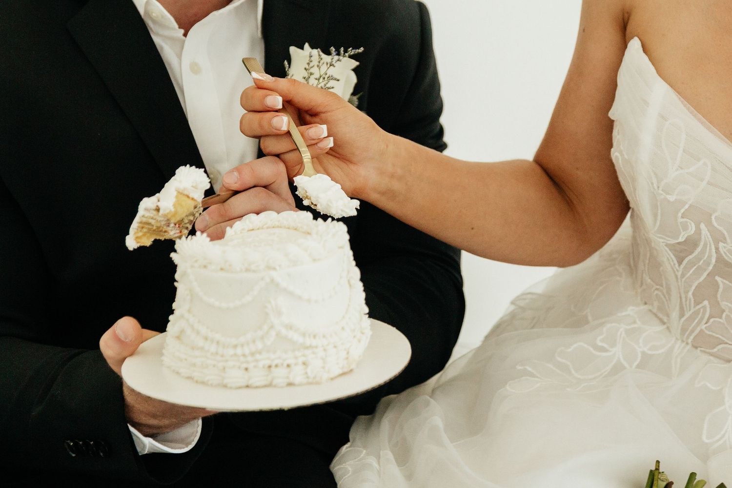 Bride and groom cutting a white wedding cake decorated with flowers and a gold cake topper.