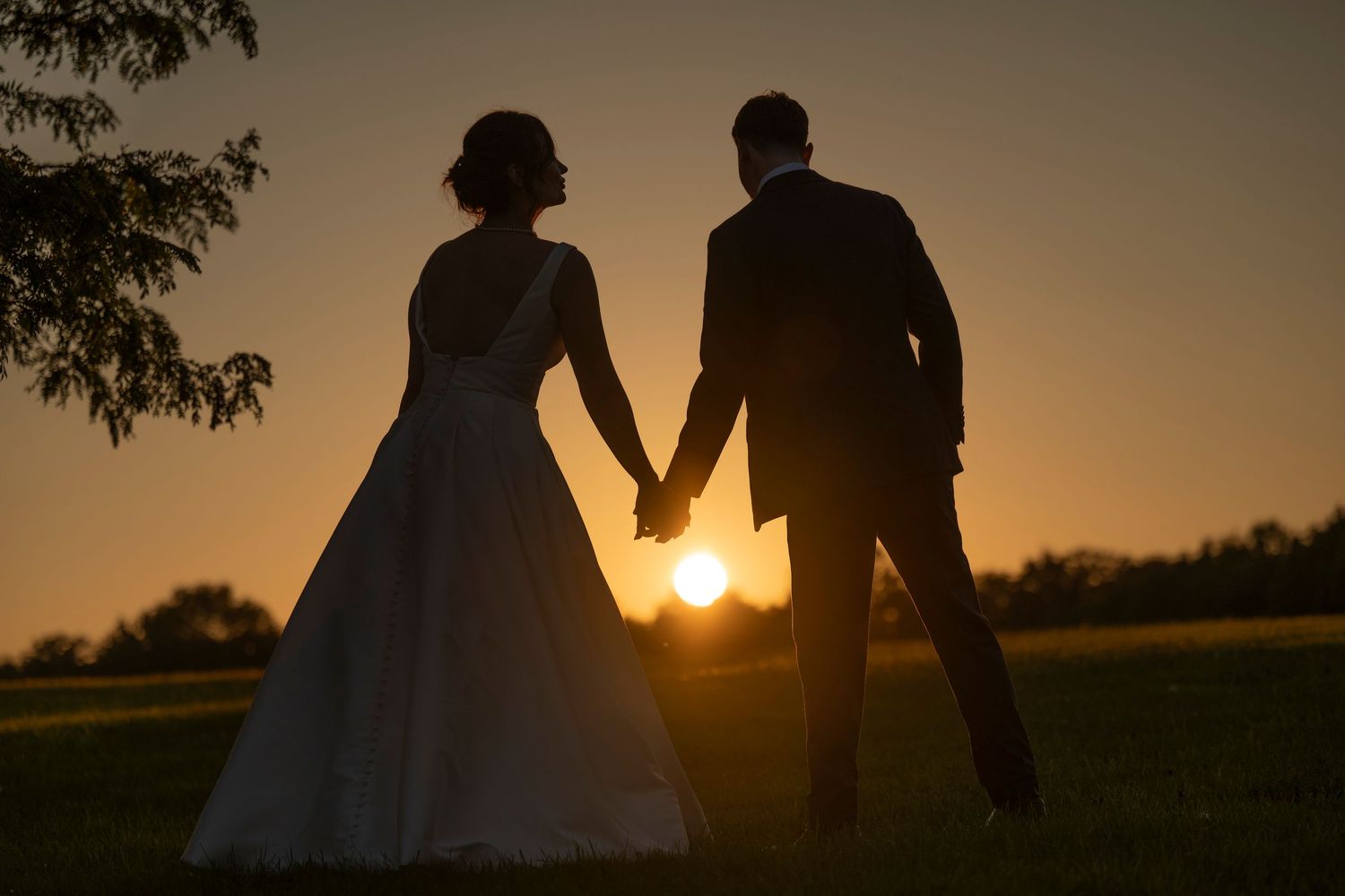 Silhouette of bride and groom holding hands at sunset on their wedding day.
