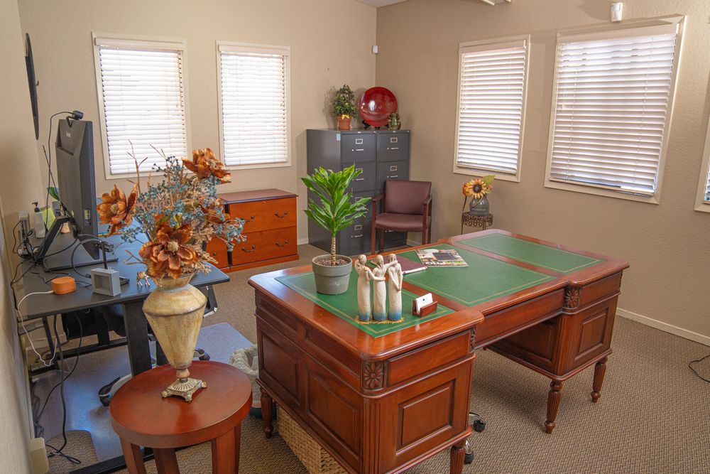 Elegant home office with cherry wood desk, green leather top, filing cabinet, and decorative floral arrangements.