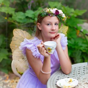 Young girl in fairy costume with floral crown holds teacup at garden tea party.