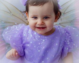 Smiling baby girl in purple fairy costume with tulle wings and lavender dress, perfect for Halloween or dress-up photos.