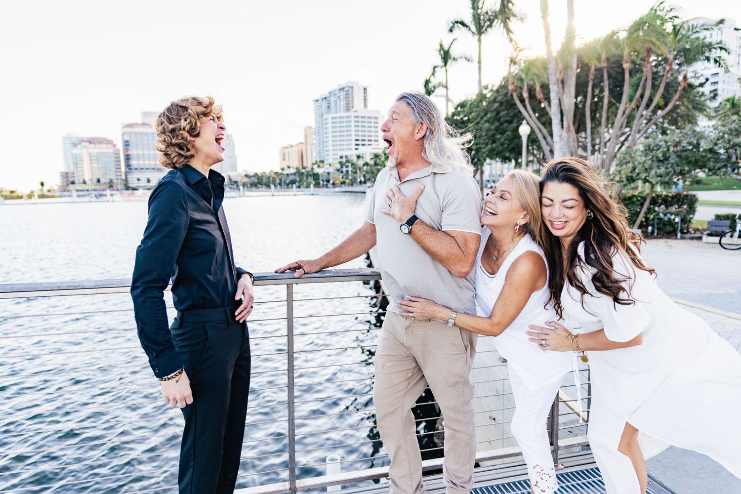 Four people laughing and posing together on a waterfront dock with a city skyline backdrop downtown west palm beach.